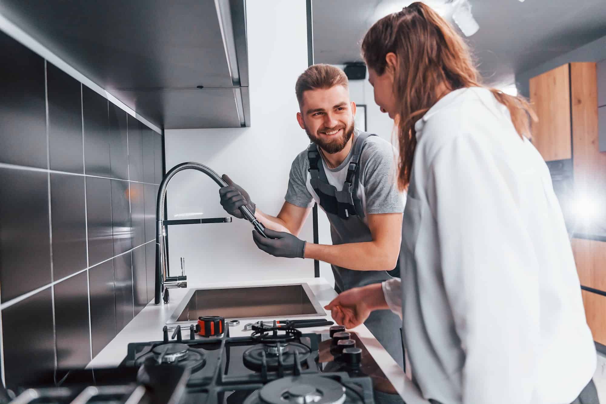 young-professional-plumber-in-grey-uniform-shows-results-of-work-for-housewife-on-the-kitchen.jpg